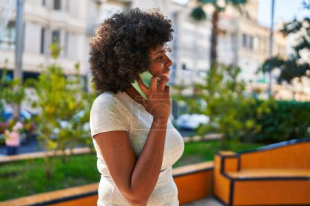 Téléchargez les photos : Femme afro-américaine souriant confiant parler sur le smartphone au parc - en image libre de droit