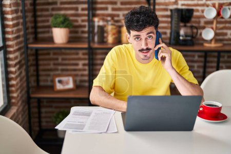 Téléchargez les photos : Young caucasian man using laptop talking on smartphone at home - en image libre de droit