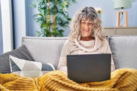 Photo for Middle age woman using laptop sitting on sofa at home - Royalty Free Image