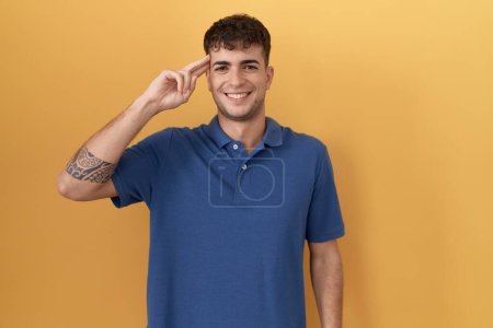 Téléchargez les photos : Jeune homme hispanique debout sur fond jaune souriant pointant vers la tête avec un doigt, bonne idée ou pensée, bonne mémoire - en image libre de droit