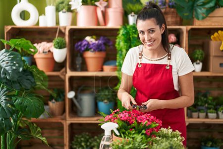 Téléchargez les photos : Jeune belle hispanique femme fleuriste couper des plantes à la boutique de fleurs - en image libre de droit