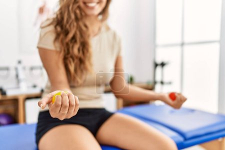 Photo for Young beautiful hispanic woman patient having rehab press balls with hands at rehab clinic - Royalty Free Image