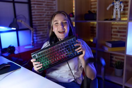 Photo for Young caucasian woman holding gamer keyboard smiling and laughing hard out loud because funny crazy joke. - Royalty Free Image