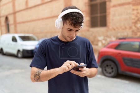 Téléchargez les photos : Jeune homme hispanique écoutant de la musique dans la rue - en image libre de droit