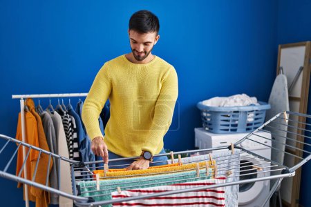Photo for Young hispanic man smiling confident hanging clothes on clothesline at laundry room - Royalty Free Image