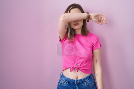 Photo for Blonde caucasian woman standing over pink background covering eyes with arm, looking serious and sad. sightless, hiding and rejection concept - Royalty Free Image