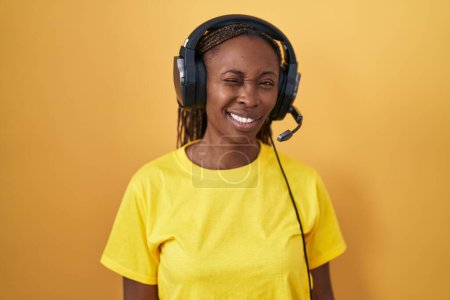 Photo for African american woman listening to music using headphones winking looking at the camera with sexy expression, cheerful and happy face. - Royalty Free Image