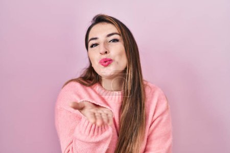 Téléchargez les photos : Jeune femme hispanique debout sur fond rose regardant la caméra souffler un baiser avec la main sur l'air étant belle et sexy. expression d'amour. - en image libre de droit