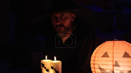 Foto de Joven calvo con traje de mago sosteniendo la lámpara de halloween de calabaza y vela en casa - Imagen libre de derechos