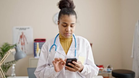 Photo for Young african american woman doctor using smartphone at clinic - Royalty Free Image
