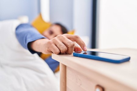 Foto de Joven hispano durmiendo en la cama apagando la alarma de smartphone en el dormitorio - Imagen libre de derechos