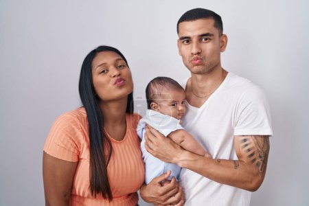 Photo for Young hispanic couple with baby standing together over isolated background looking at the camera blowing a kiss on air being lovely and sexy. love expression. - Royalty Free Image
