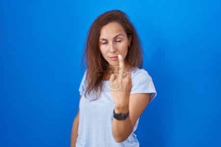 Foto de Brunette woman standing over blue background showing middle finger, impolite and rude fuck off expression - Imagen libre de derechos