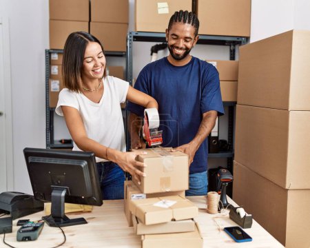 Téléchargez les photos : Man and woman business partners packing package using tape at storehouse - en image libre de droit