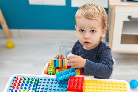 Téléchargez les photos : Adorable bambin blond jouant avec des blocs de construction assis sur la table à la maternelle - en image libre de droit