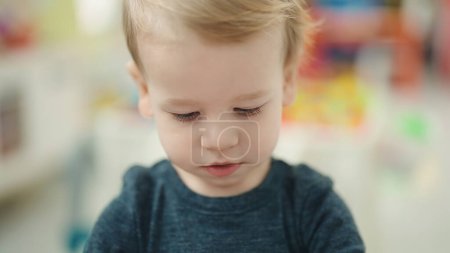 Foto de Adorable niño rubio de pie con expresión relajada en el jardín de infantes - Imagen libre de derechos