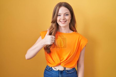 Photo for Caucasian woman standing over yellow background doing happy thumbs up gesture with hand. approving expression looking at the camera showing success. - Royalty Free Image