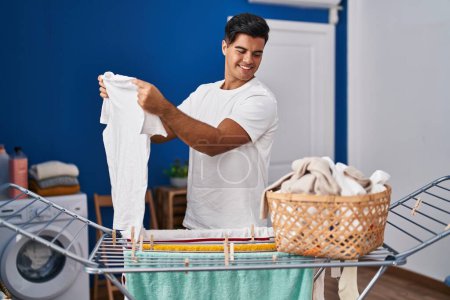 Photo for Young hispanic man smiling confident hanging clothes on clothesline at laundry room - Royalty Free Image