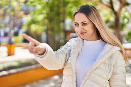 Foto de Mujer joven sonriendo confiada señalando con el dedo en el parque - Imagen libre de derechos