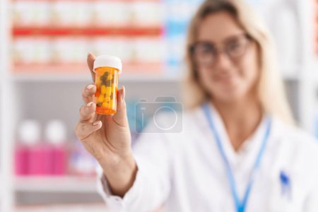 Foto de Young blonde woman pharmacist smiling confident holding pills bottle at pharmacy - Imagen libre de derechos