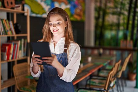 Téléchargez les photos : Young caucasian woman waitress smiling confident using touchpad at restaurant - en image libre de droit
