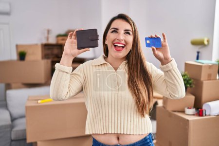 Photo for Young hispanic woman moving to a new home holding wallet and credit card smiling and laughing hard out loud because funny crazy joke. - Royalty Free Image