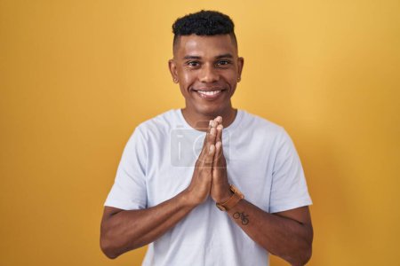 Photo for Young hispanic man standing over yellow background praying with hands together asking for forgiveness smiling confident. - Royalty Free Image