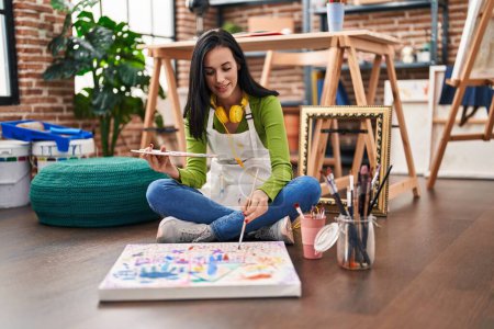 Foto de Joven mujer caucásica artista sonriendo confiado sentado en el piso de dibujo en el estudio de arte - Imagen libre de derechos