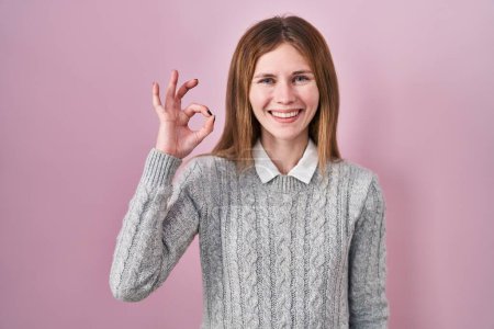 Téléchargez les photos : Belle femme debout sur fond rose souriant positif faire ok signe avec la main et les doigts. expression réussie. - en image libre de droit
