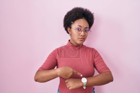 Photo for Beautiful african woman with curly hair standing over pink background in hurry pointing to watch time, impatience, upset and angry for deadline delay - Royalty Free Image