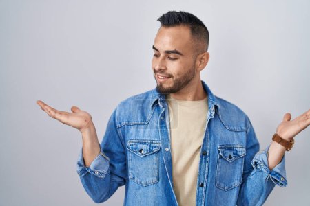 Téléchargez les photos : Jeune homme hispanique debout sur fond isolé souriant montrant les paumes ouvertes des deux mains, présentant et comparant la publicité et l'équilibre - en image libre de droit