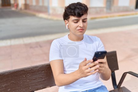 Téléchargez les photos : Non binary man listening to music sitting on bench at park - en image libre de droit