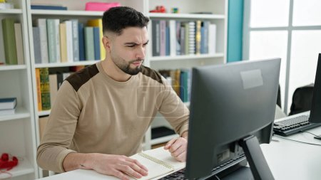 Téléchargez les photos : Jeune homme arabe étudiant à l'aide d'un ordinateur étudiant avec l'expression du doute à l'université classe - en image libre de droit