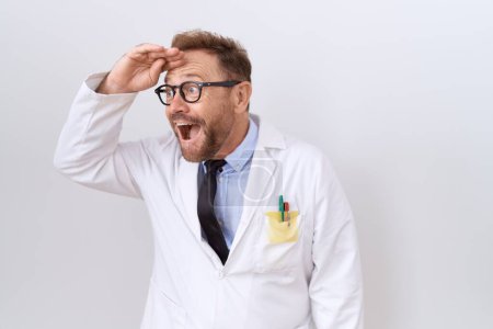 Téléchargez les photos : Médecin d'âge moyen homme barbe vêtu d'un manteau blanc très heureux et souriant regardant loin avec la main au-dessus de la tête. concept de recherche. - en image libre de droit