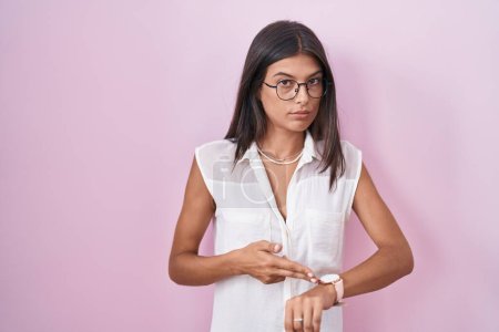 Photo for Brunette young woman standing over pink background wearing glasses in hurry pointing to watch time, impatience, upset and angry for deadline delay - Royalty Free Image