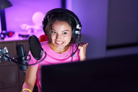 Photo for Hispanic young woman playing video games pointing thumb up to the side smiling happy with open mouth - Royalty Free Image