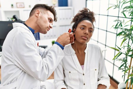 Téléchargez les photos : Homme et femme portant l'uniforme de médecin examinant l'oreille à l'aide d'un otoscope à la clinique - en image libre de droit