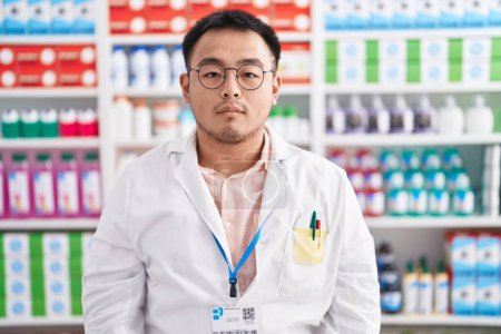 Photo for Chinese young man working at pharmacy drugstore relaxed with serious expression on face. simple and natural looking at the camera. - Royalty Free Image
