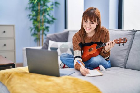 Photo for Young woman composing song playing ukelele at home - Royalty Free Image