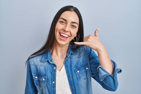 Téléchargez les photos : Femme hispanique debout sur fond bleu souriant faire geste de téléphone avec la main et les doigts comme parler au téléphone. communiquer les concepts. - en image libre de droit