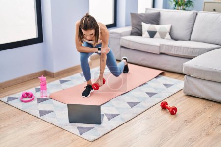 Photo for Young beautiful hispanic woman having online training with dumbbells at home - Royalty Free Image