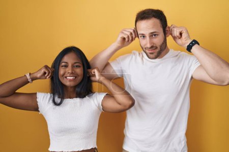 Photo for Interracial couple standing over yellow background smiling pulling ears with fingers, funny gesture. audition problem - Royalty Free Image