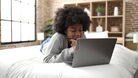Téléchargez les photos : African american woman using laptop lying on bed at bedroom - en image libre de droit