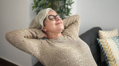Téléchargez les photos : Middle age woman with grey hair relaxed with hands on head sitting on sofa at home - en image libre de droit