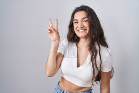Photo for Young teenager girl standing over white background smiling looking to the camera showing fingers doing victory sign. number two. - Royalty Free Image