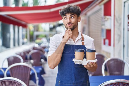 Téléchargez les photos : Arab man with beard wearing waiter apron at restaurant terrace serious face thinking about question with hand on chin, thoughtful about confusing idea - en image libre de droit