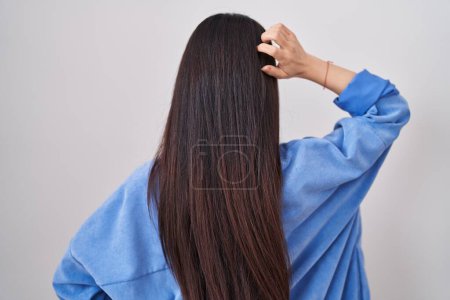 Téléchargez les photos : Jeune femme chinoise debout sur fond blanc vers l'arrière pensant au doute avec la main sur la tête - en image libre de droit