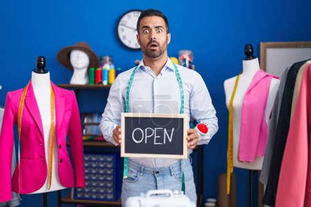 Photo for Hispanic man with beard working as dressmaker at atelier in shock face, looking skeptical and sarcastic, surprised with open mouth - Royalty Free Image