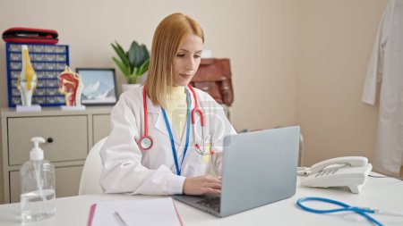 Foto de Young blonde woman doctor using laptop working at clinic - Imagen libre de derechos