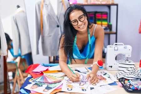 Téléchargez les photos : Jeune belle femme latine tailleur souriant conception de vêtements de dessin confiant sur ordinateur portable chez le fleuriste - en image libre de droit